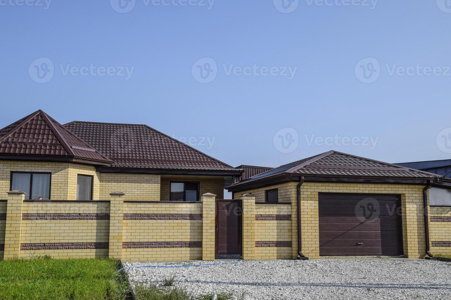 Brick house with a fence and gates. View of a new built-up fence and a house made of bricks and corrugated metal. photo