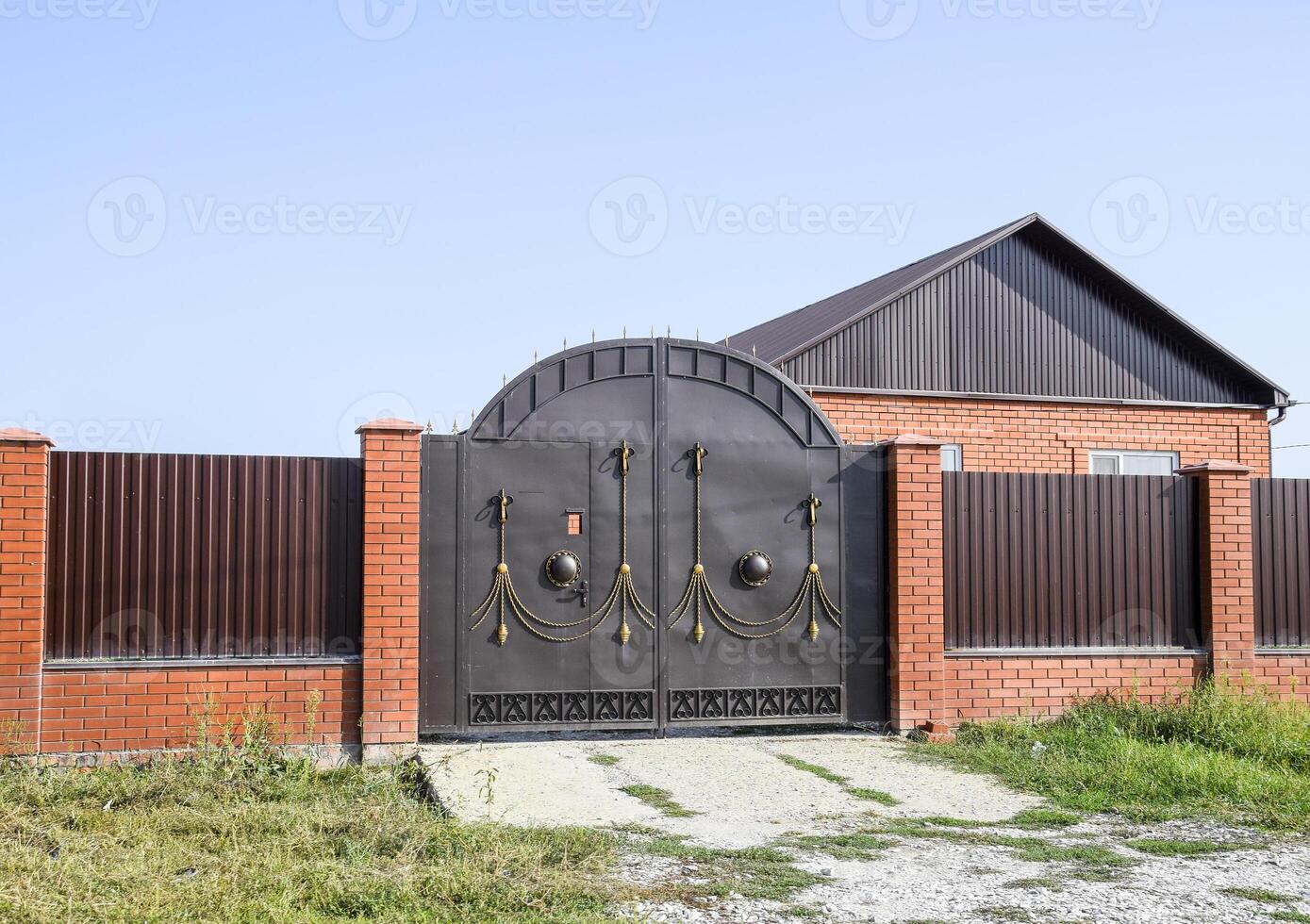 Brick house with a fence and gates. View of a new built-up fence and a house made of bricks and corrugated metal. photo