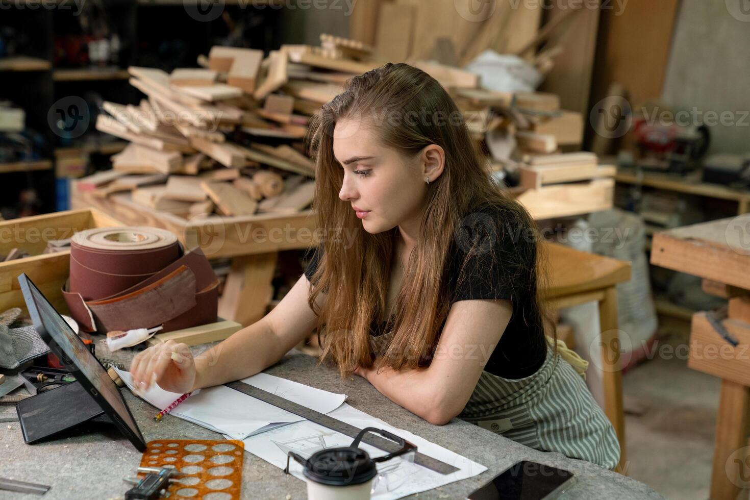 un joven mujer es formación a ser un carpintero en el taller. ella trabajos con un ordenador portátil computadora en un madera taller. hembra carpintero contacto clientes por teléfono inteligente SME pedidos, puesta en marcha y pequeño foto