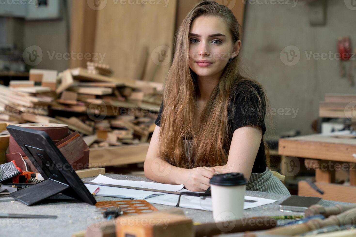 un joven mujer es formación a ser un carpintero en el taller. ella trabajos con un ordenador portátil computadora en un madera taller. hembra carpintero contacto clientes por teléfono inteligente SME pedidos, puesta en marcha y pequeño foto