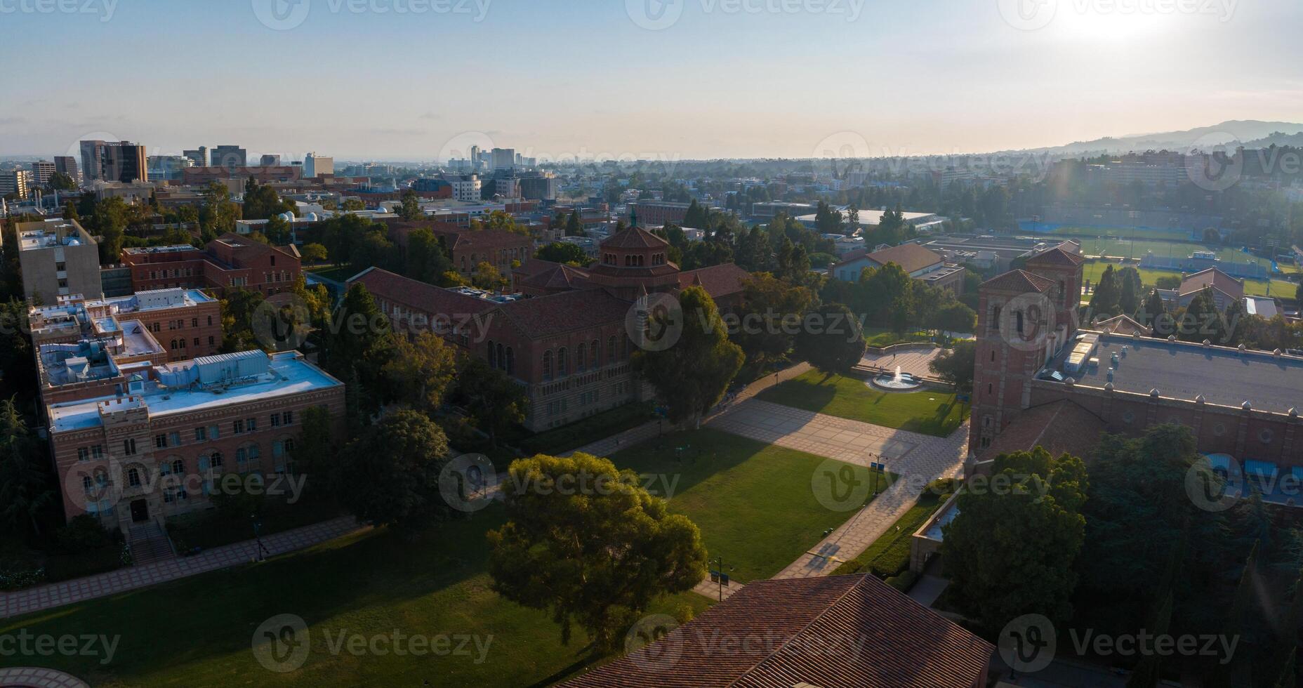 Aerial View of Historic and Modern University Campus at Sunrise with Green Lawns and Cityscape Background photo