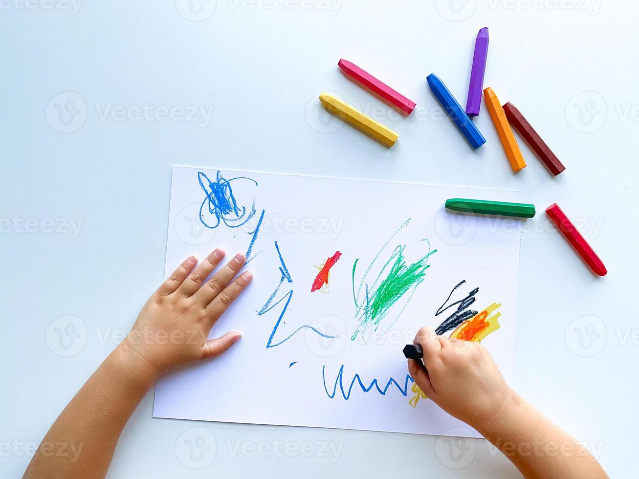 pequeño niño sorteos con pastel lápices de color en blanco mesa. foto