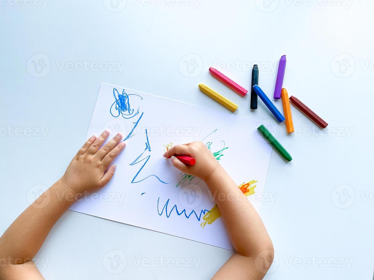 pequeño niño sorteos con pastel lápices de color en blanco mesa. foto
