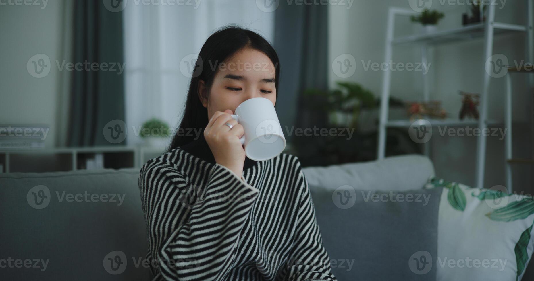 retrato de relajante joven mujer participación taza disfrutar oler café o té y Bebiendo con felicidad en Mañana mientras sentar en sofá en vivo habitación, gratis tiempo, toma descanso en casa, sonriendo foto