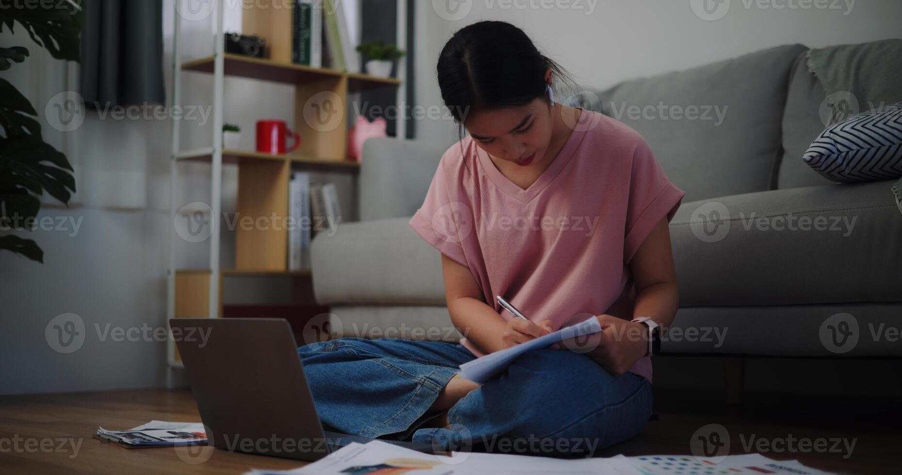 retrato de joven mujer sentado en el piso trabajando con un ordenador portátil y comprobación papel de trabajo a hogar oficina. foto