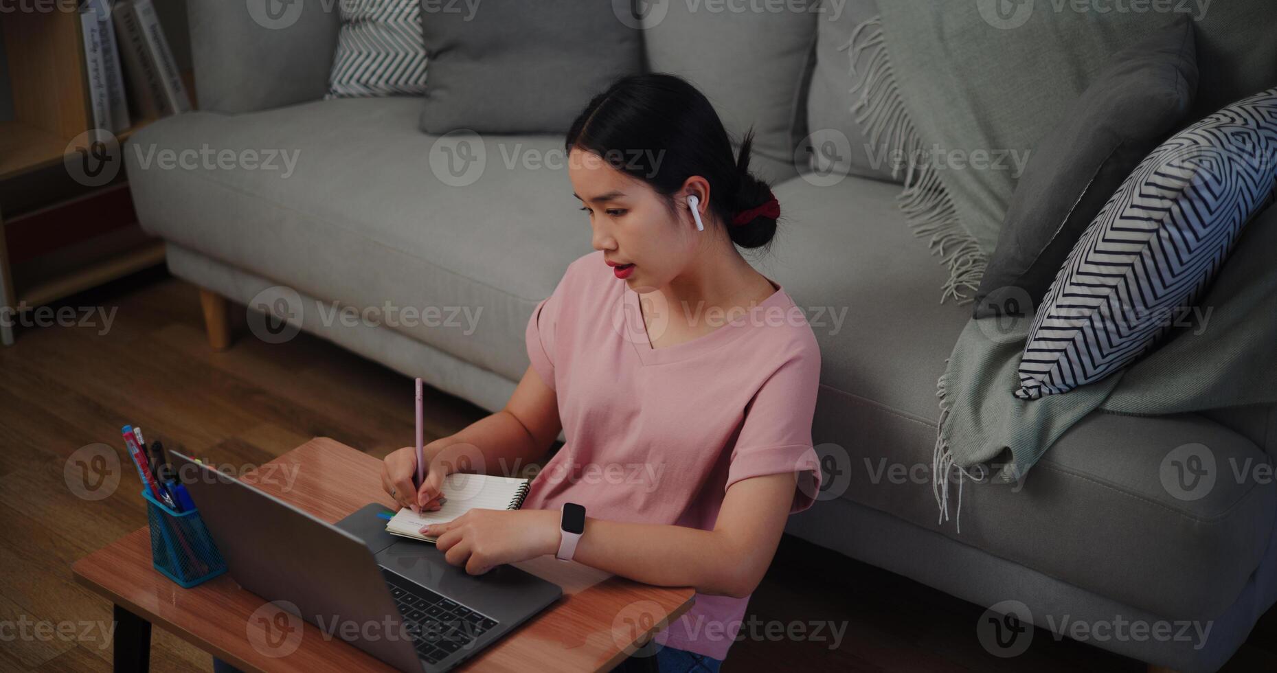 Portrait of Young woman sitting on the floor leaning against a sofa working with a laptop and take notes in a notebook at home office. photo