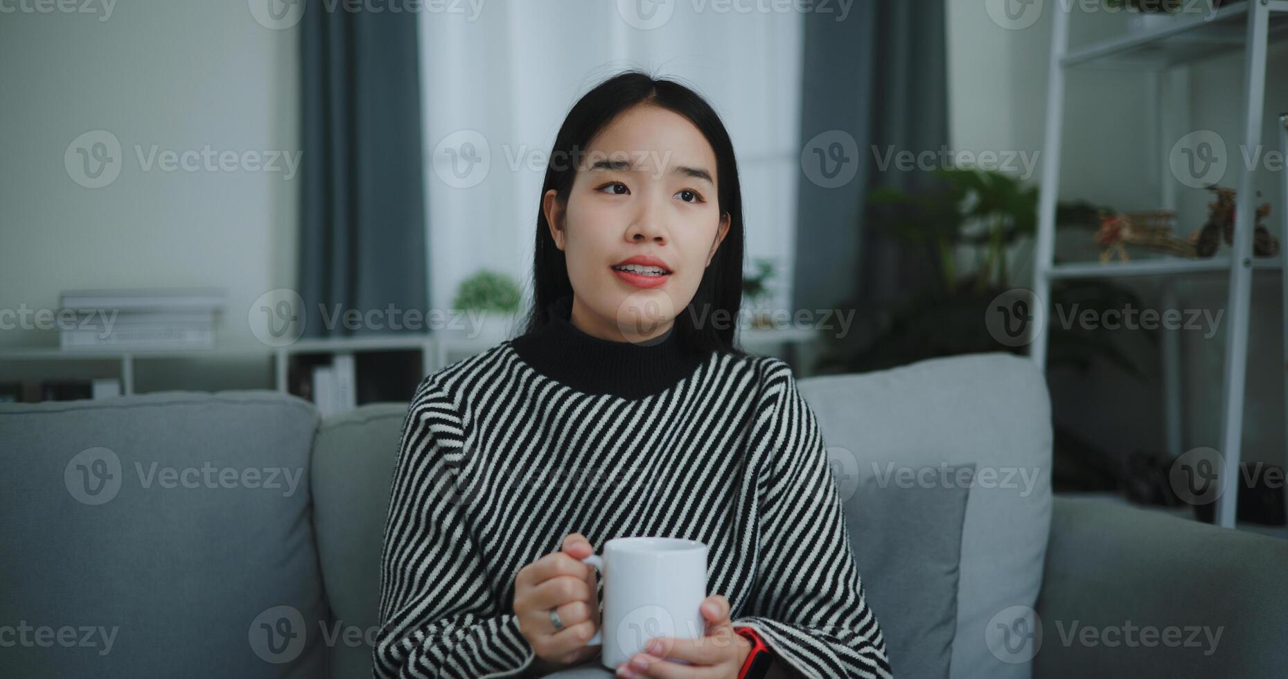 retrato de relajante joven mujer participación taza disfrutar oler café o té y Bebiendo con felicidad en Mañana mientras sentar en sofá en vivo habitación, gratis tiempo, toma descanso en casa, sonriendo foto