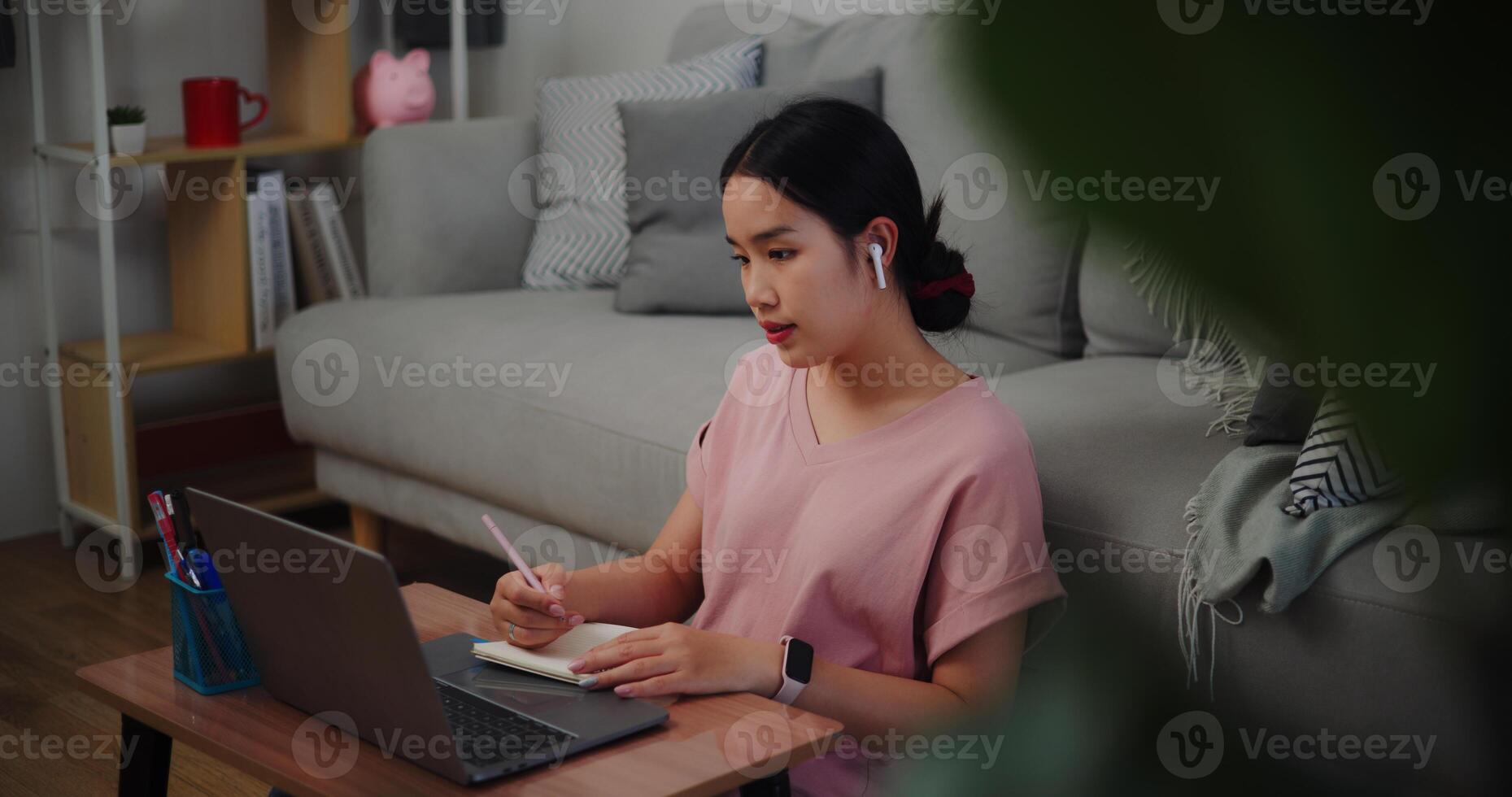 Portrait of Young woman sitting on the floor leaning against a sofa working with a laptop and take notes in a notebook at home office. photo