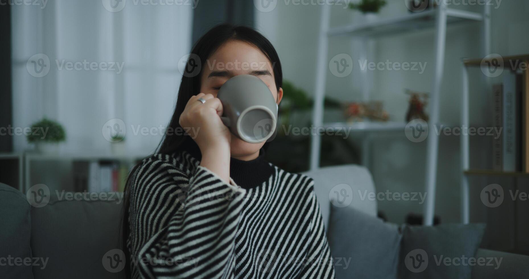 retrato de relajante joven mujer participación taza disfrutar oler café o té y Bebiendo con felicidad en Mañana mientras sentar en sofá en vivo habitación, gratis tiempo, toma descanso en casa, sonriendo foto