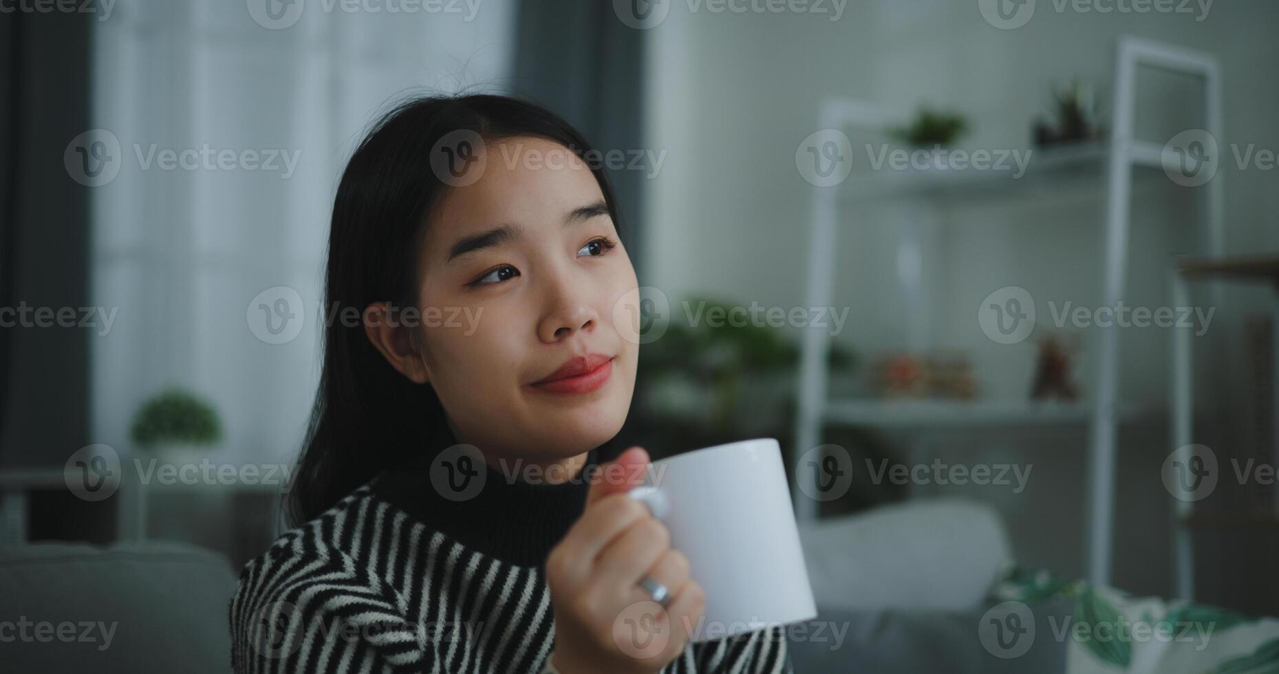 retrato de relajante joven mujer participación taza disfrutar oler café o té y Bebiendo con felicidad en Mañana mientras sentar en sofá en vivo habitación, gratis tiempo, toma descanso en casa, sonriendo foto