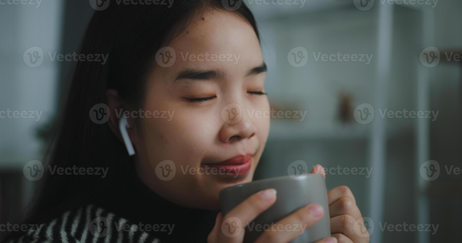 Portrait of Happy young asian woman enjoy listening to the music with wireless headphones while sitting drink coffee on sofa in living room at home, Leisure and lifestyle,Free time photo