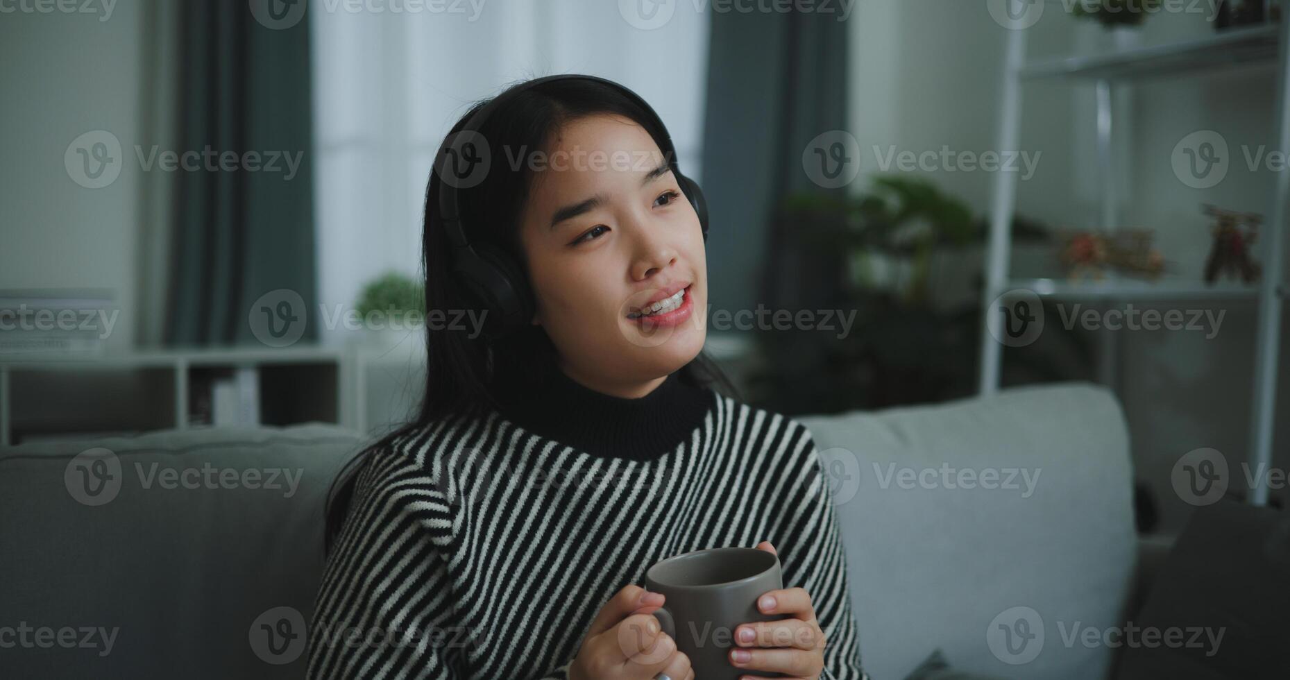 Portrait of Happy young asian woman enjoy listening to the music with wireless headphones while sitting drink coffee on sofa in living room at home, Leisure and lifestyle,Free time photo