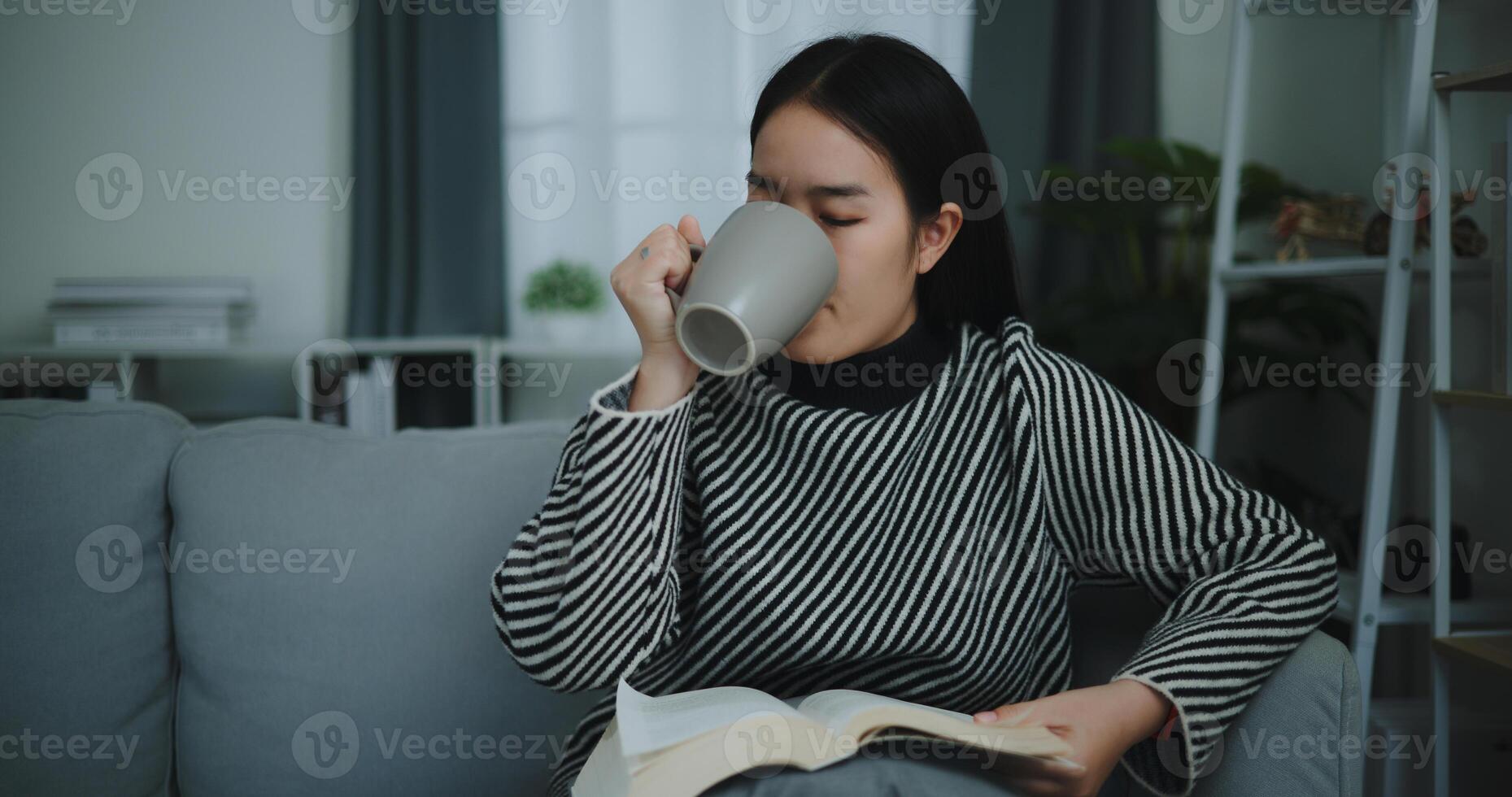 Portrait of Happy young asian woman drinking morning coffee or tea and reading in living room at home on weekend. Leisure and lifestyle,Free time photo