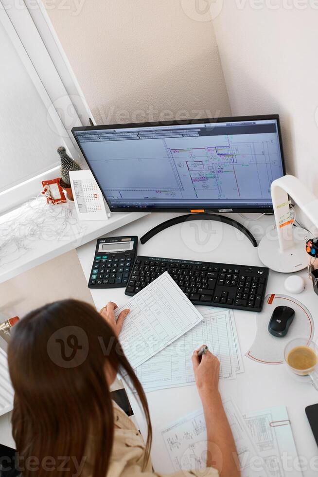 Portrait of a remote worker. An adult woman sits at a table in front of a computer and draws up a costly estimate. Confident young lady freelancer working from home. photo