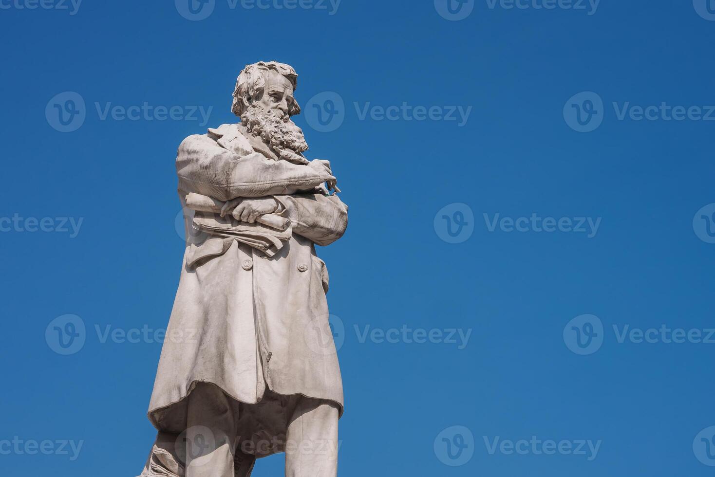 Contemplative bearded man statue in long coat against blue sky backdrop in Venice. photo