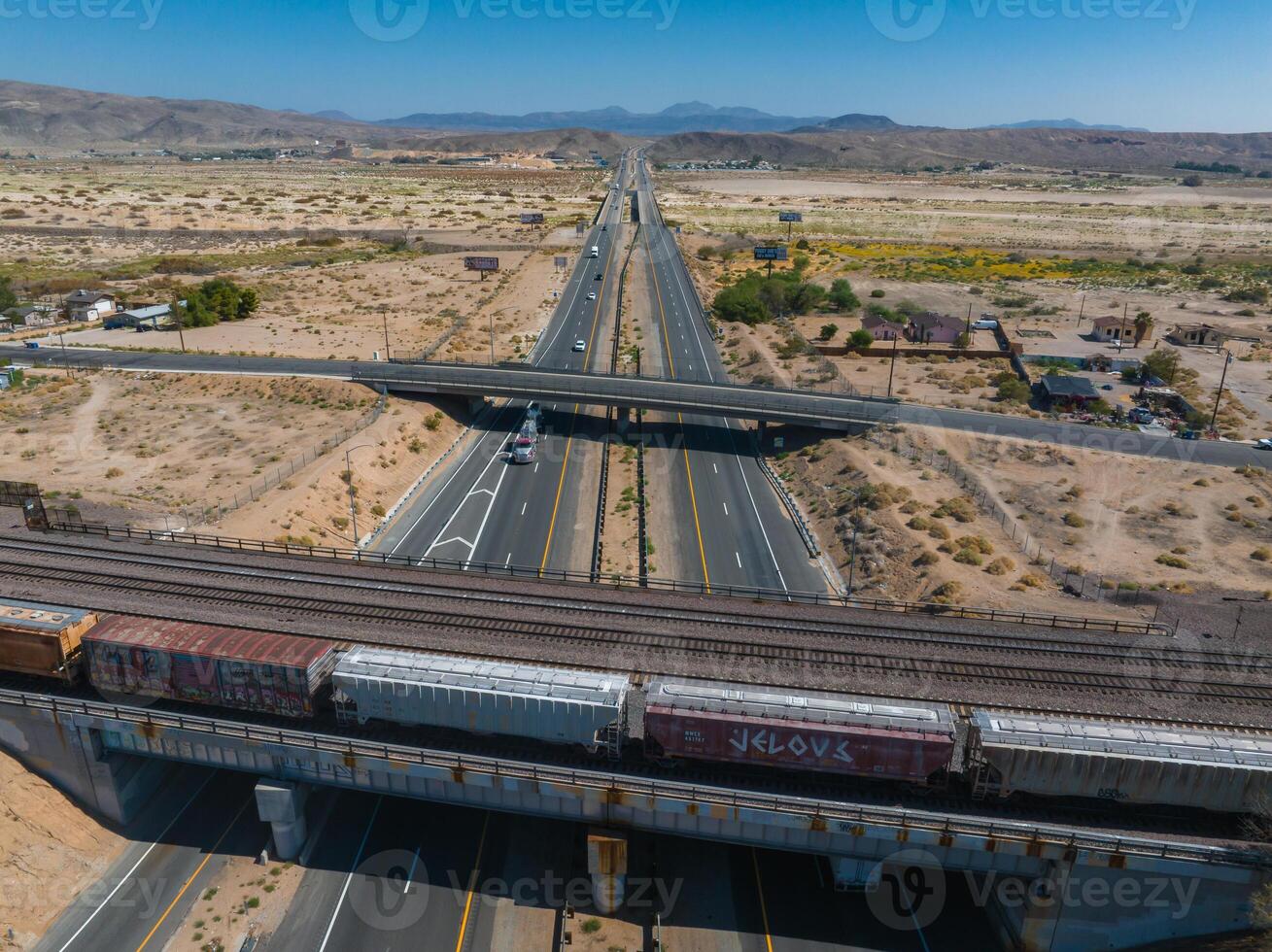 Aerial View of Desert Highway Interchange with Train Tracks and Rugged Mountains Under Clear Blue Sky photo