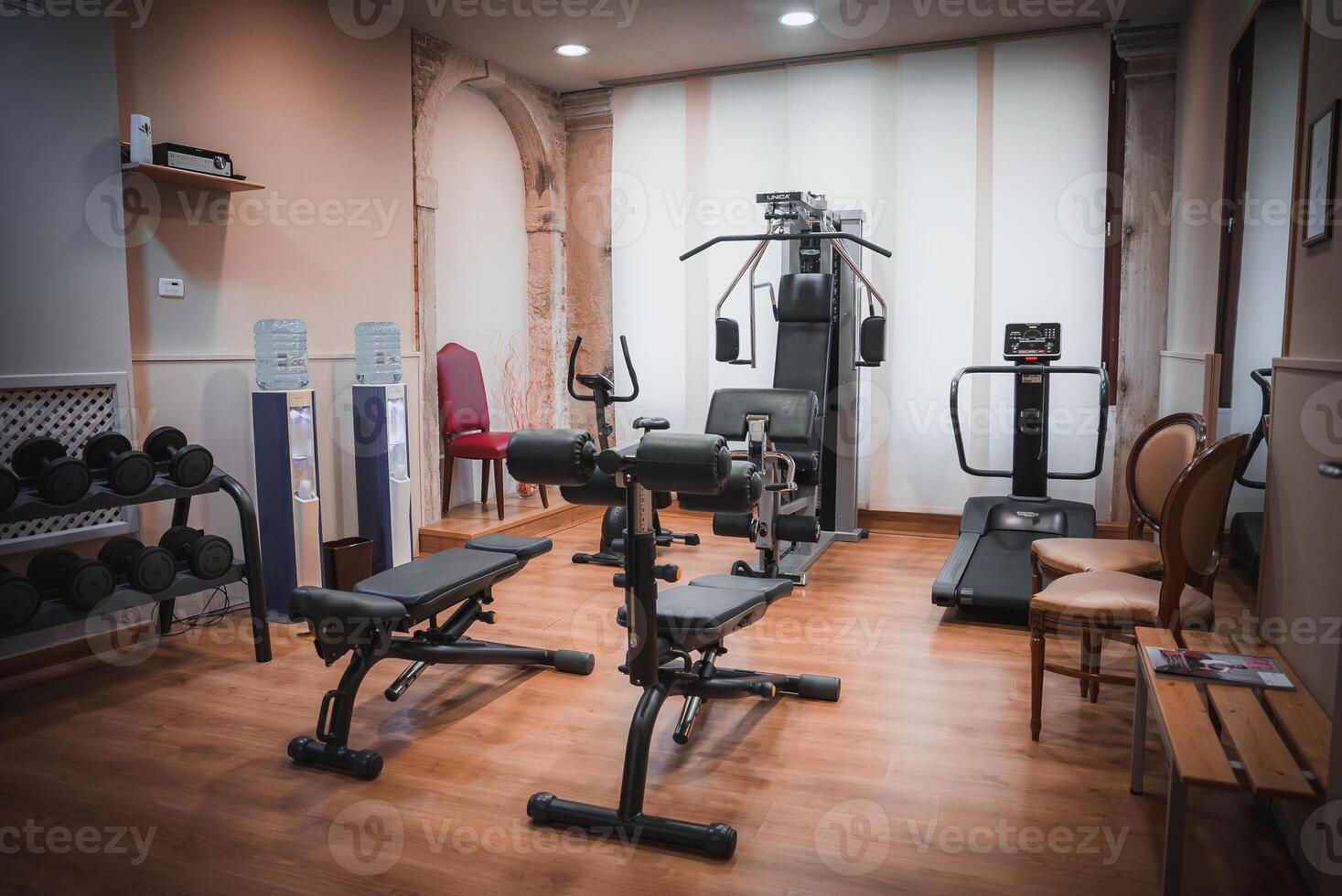 Modern gym room with rowing machine, exercise equipment, and chair in side angle view. photo