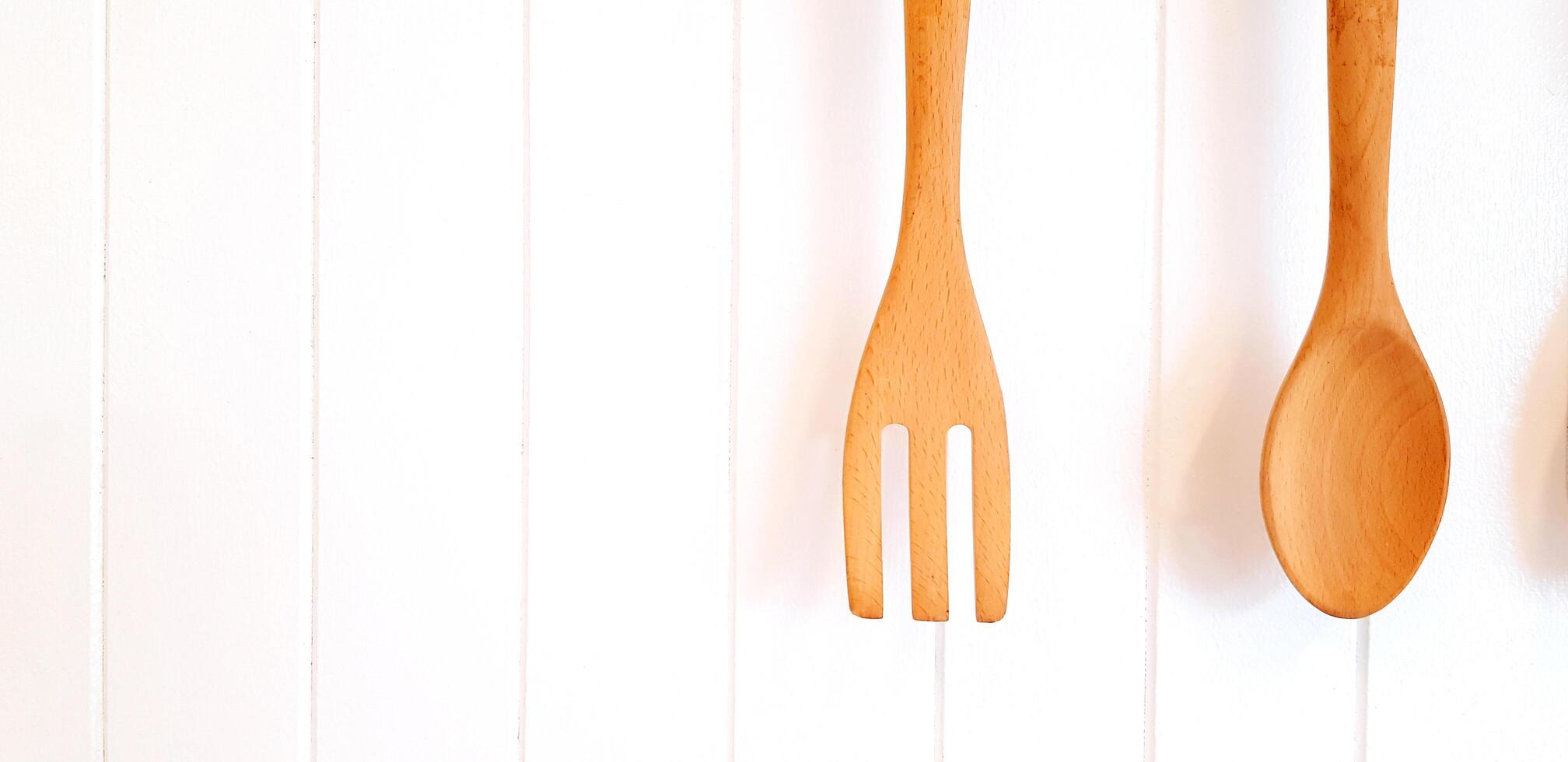 Brown wooden fork and spoon hanging and isolated on white wooden background with copy space. Kitchen utensil and Vintage object concept photo
