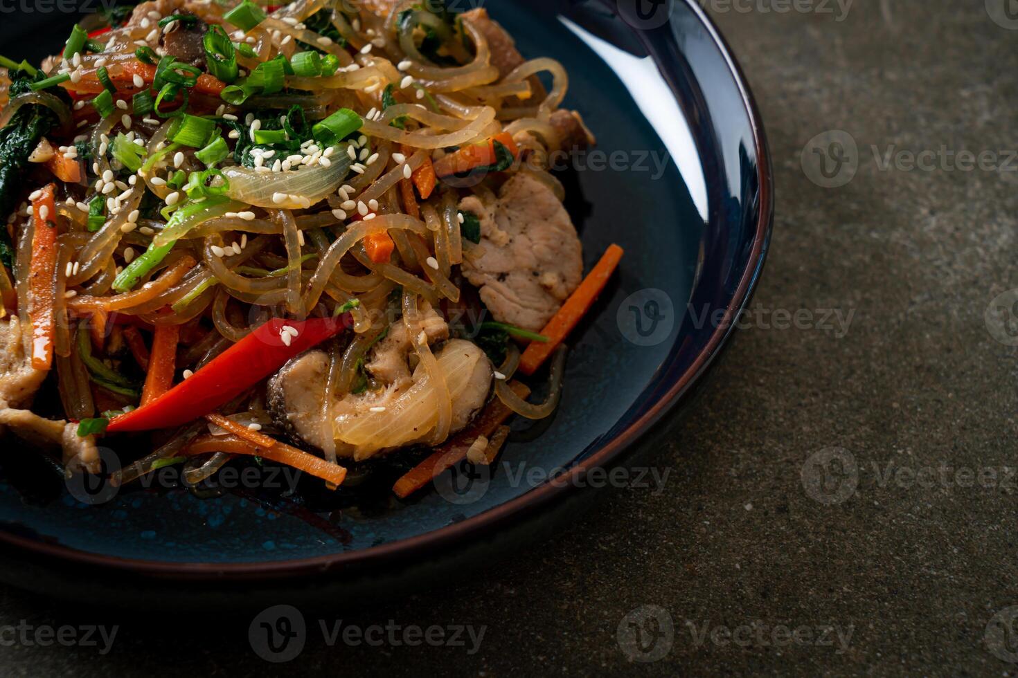 japchae or stir-fried Korean vermicelli noodles with vegetables and pork topped with white sesame photo