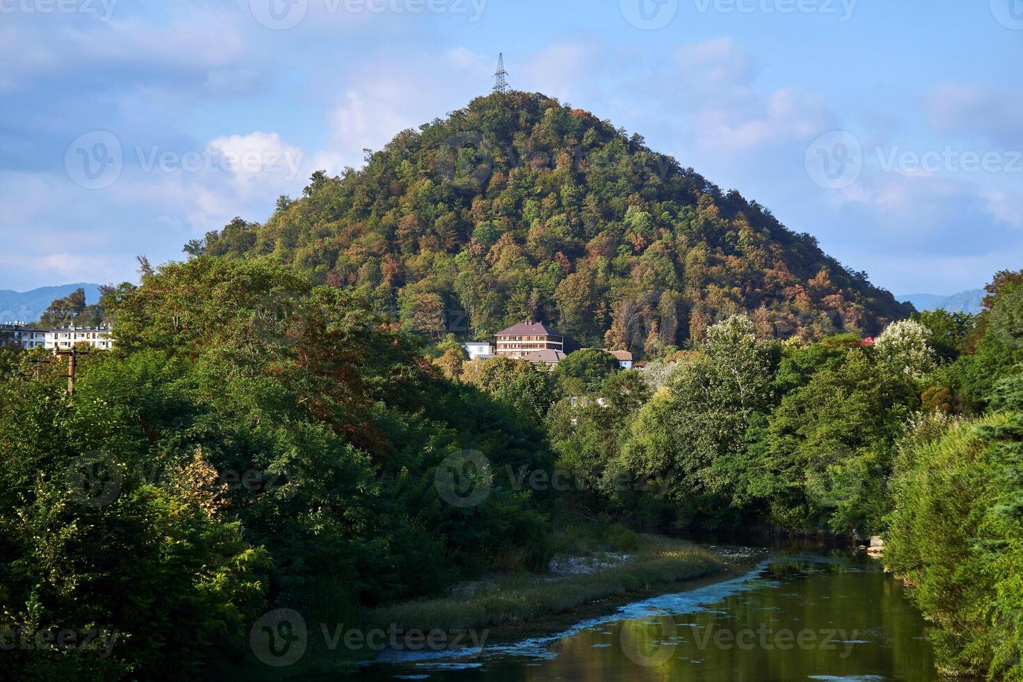 landscape with a hill, a river and a power transmission tower at the top photo