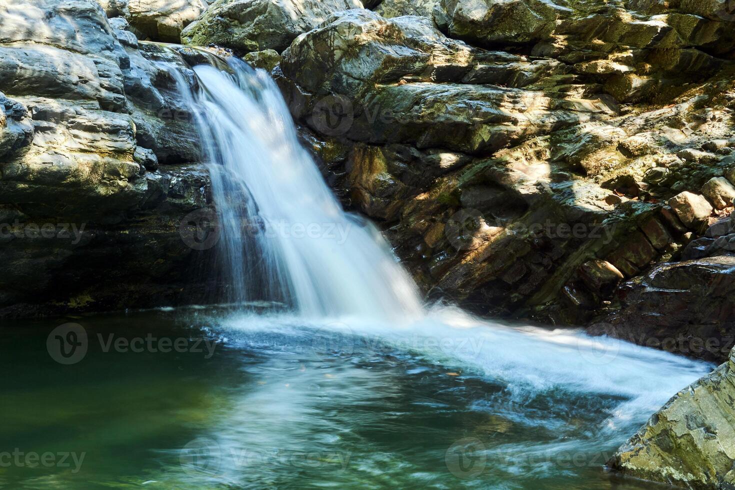 small mountain waterfall among the rocks, the water is blurred in motion photo