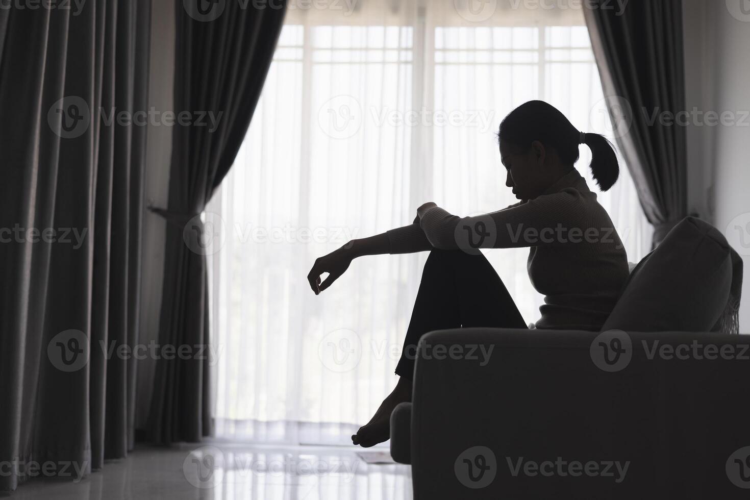 Silhouette of a person suffering from depression in the house, Depressed woman sitting alone on the Sofa feel stress, sad and worried in the dark room. person are stressed. photo