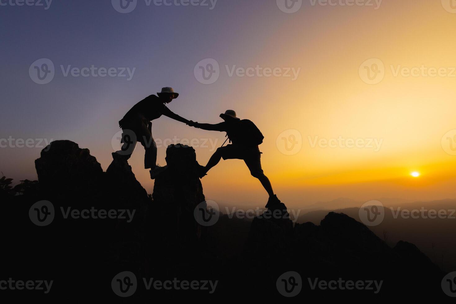 siluetas de dos personas alpinismo en montaña y Ayudar. trabajo en equipo de dos hombres caminante Ayudar cada otro en parte superior de montaña alpinismo equipo hermosa amanecer. ayuda y asistencia concepto. foto