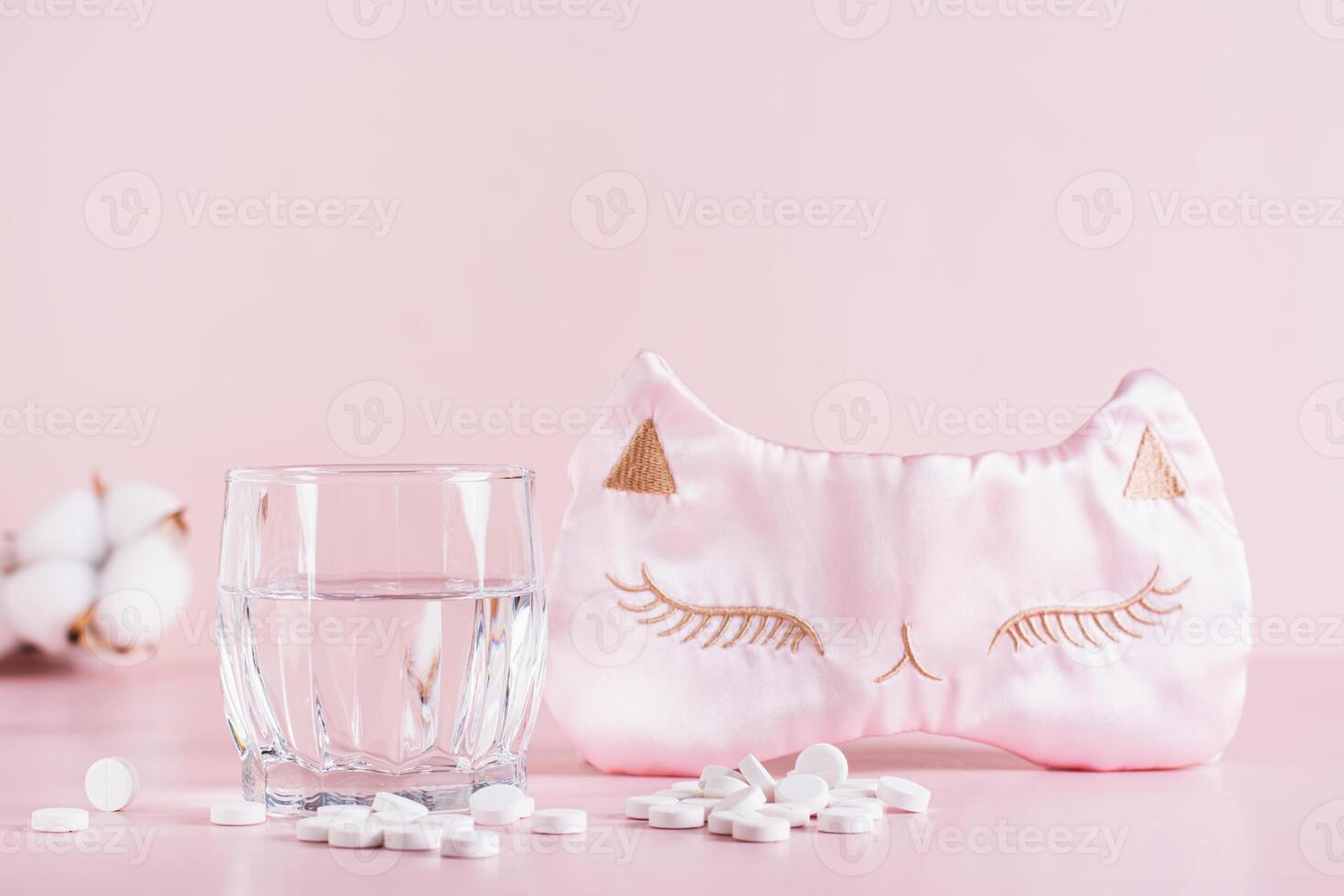 Sleeping pills, a glass of water and a sleep mask on a pink background photo