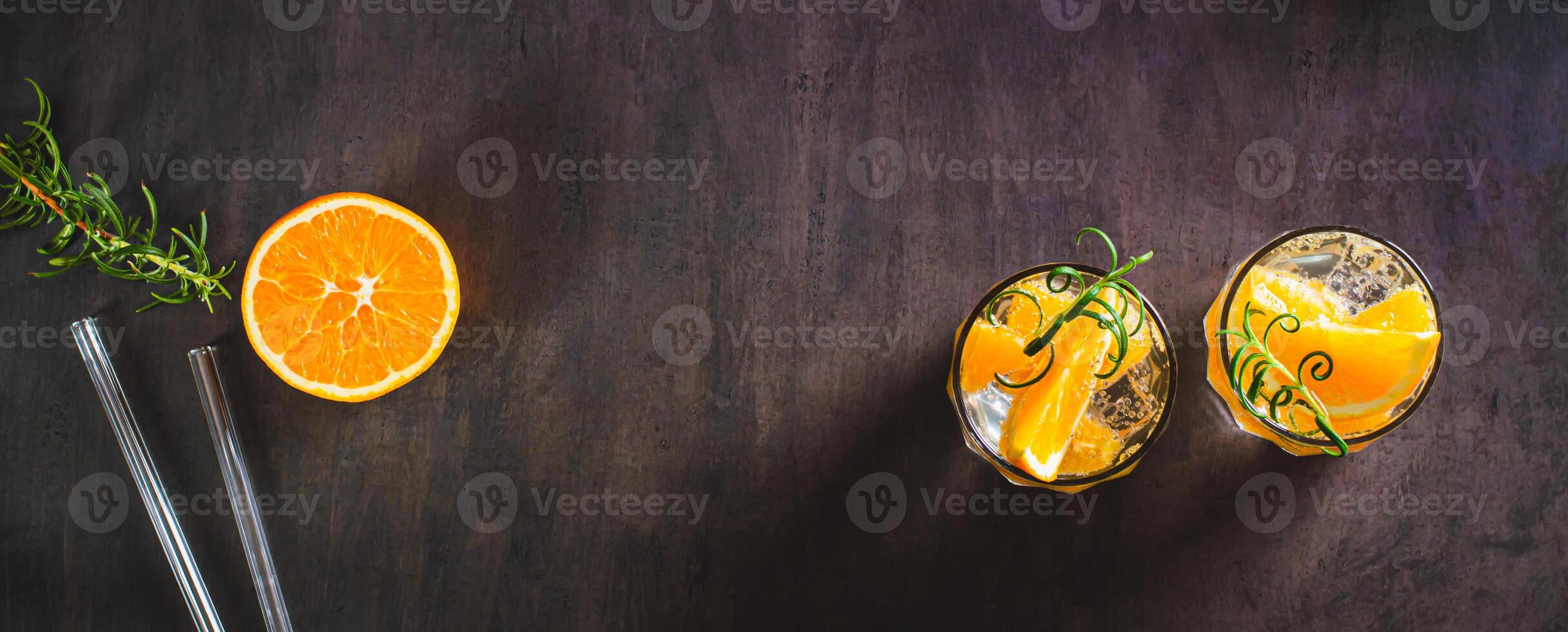 Hard seltzer with ice, orange and rosemary in glasses on the table top view web banner photo