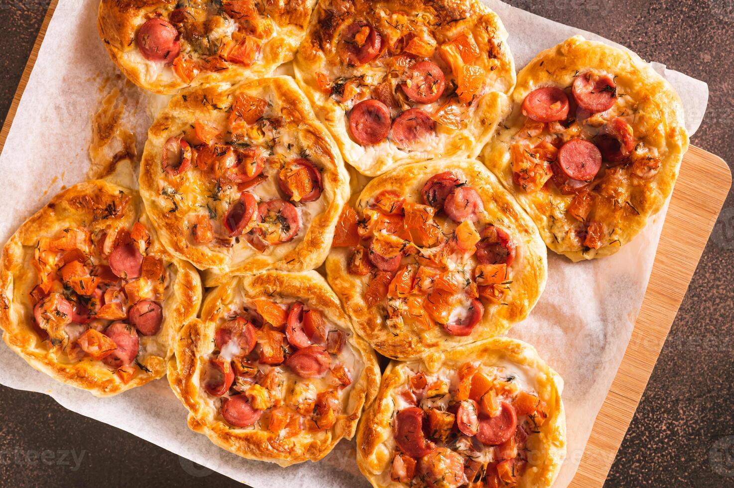 Close up of pizza pot pies with tomatoes, cheese and sausages on a wooden board top view photo