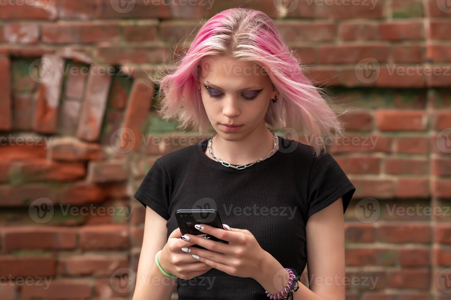 teen girl writes or reads a message using the phone against the background of an old wall photo