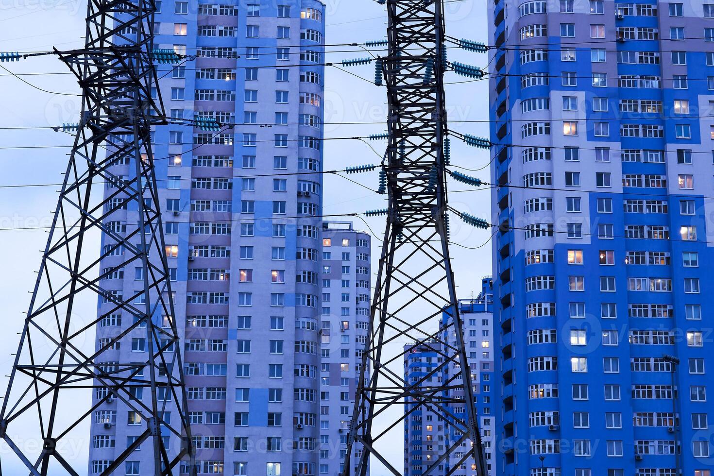 power line supports against the background of multi-storey residential buildings in the evening illumination photo