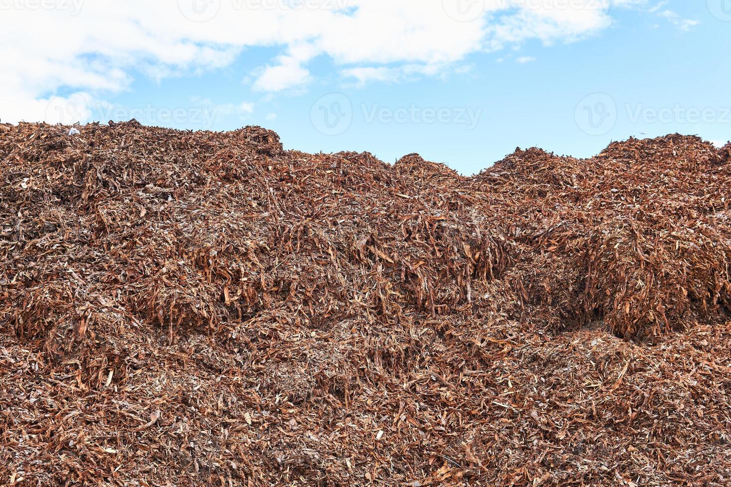 heap of tree bark removed from logs at a woodworking factory against sky photo