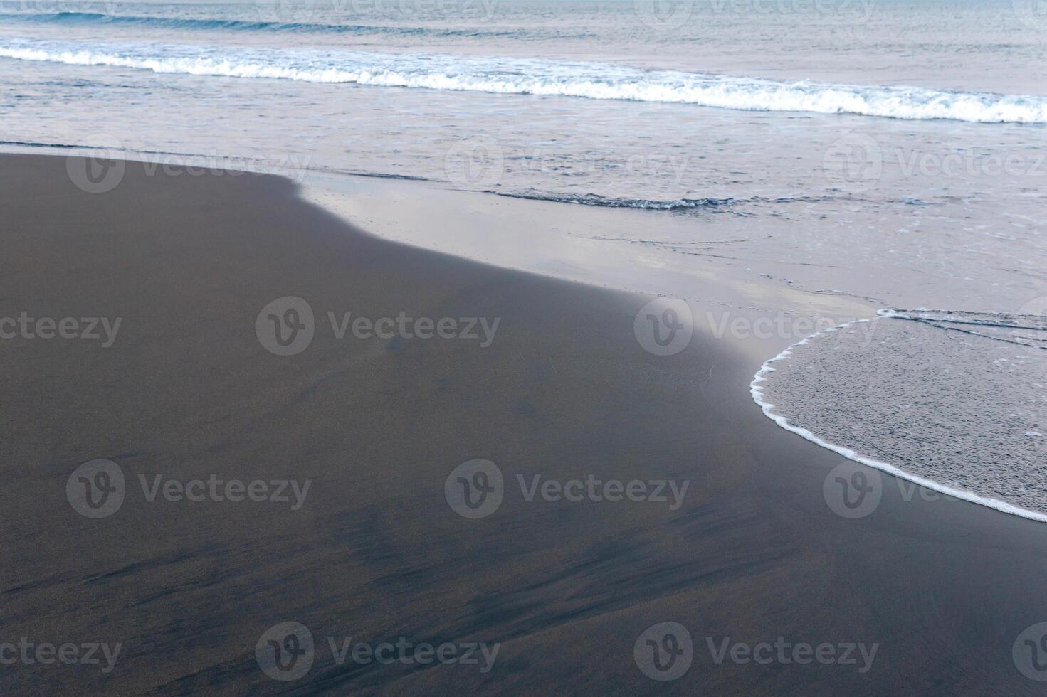 ocean beach with black volcanic sand, the sky is reflected in the rolled back wave of the surf photo