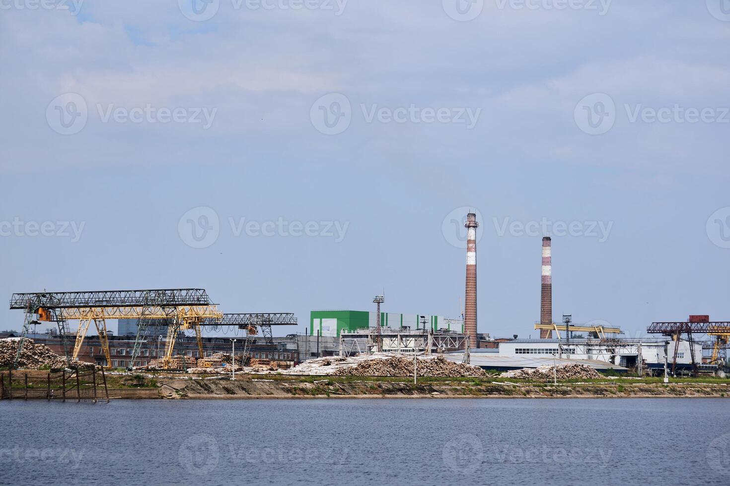 industrial landscape, pulp and paper mill with stacks of logs on the river bank photo