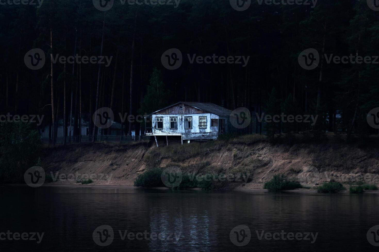 abandonado arruinado casa en un oscuro enselvado banco casi colapsado dentro el río foto