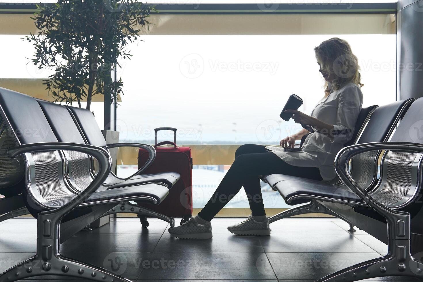 woman traveler with baggage sits in the waiting room of the airport and is waiting for the flight photo