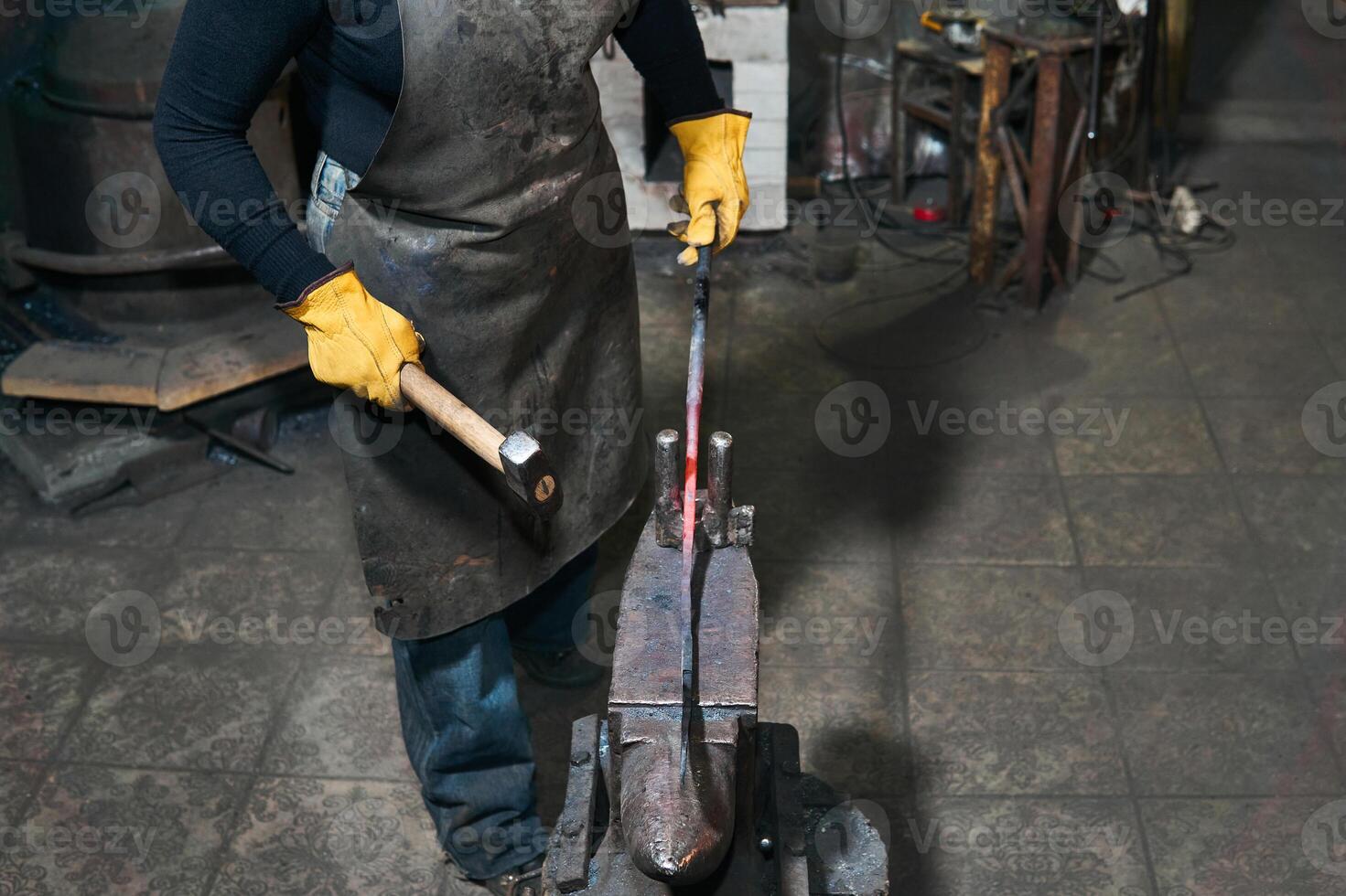 female hands forge a hot metal billet on the anvil in a traditional forge photo