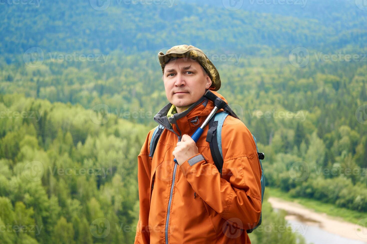 portrait of a man geologist with a backpack and a geological hammer against the wooded mountain landscape photo