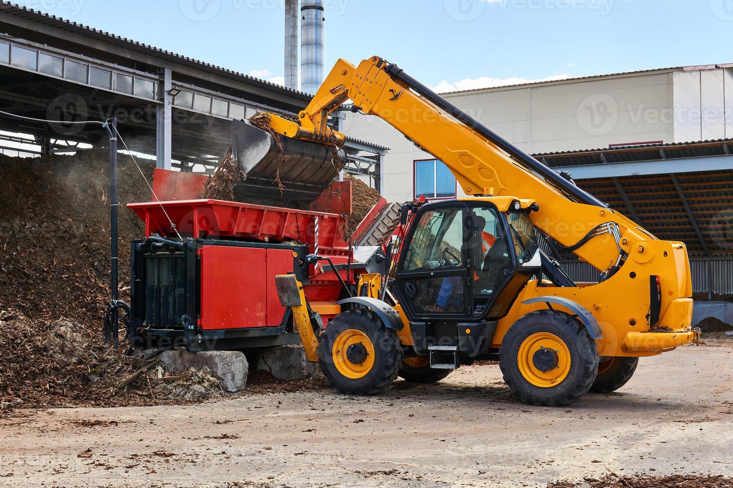 bucket loader loads tree bark into an industrial woodchipper photo