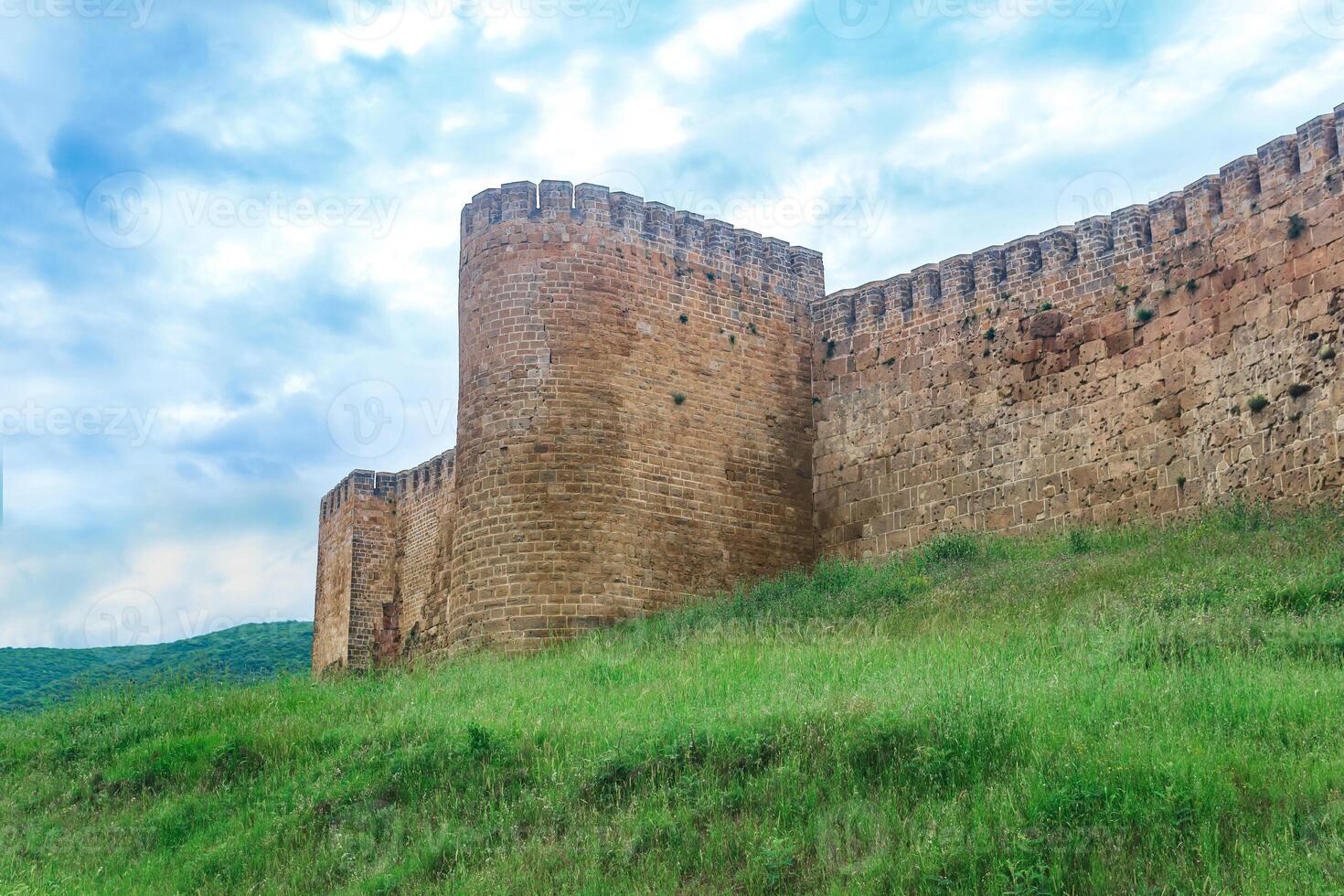 wall of a medieval fortress above a rampart overgrown with grass against the hills and sky, Naryn-Kala citadel in Derbent photo