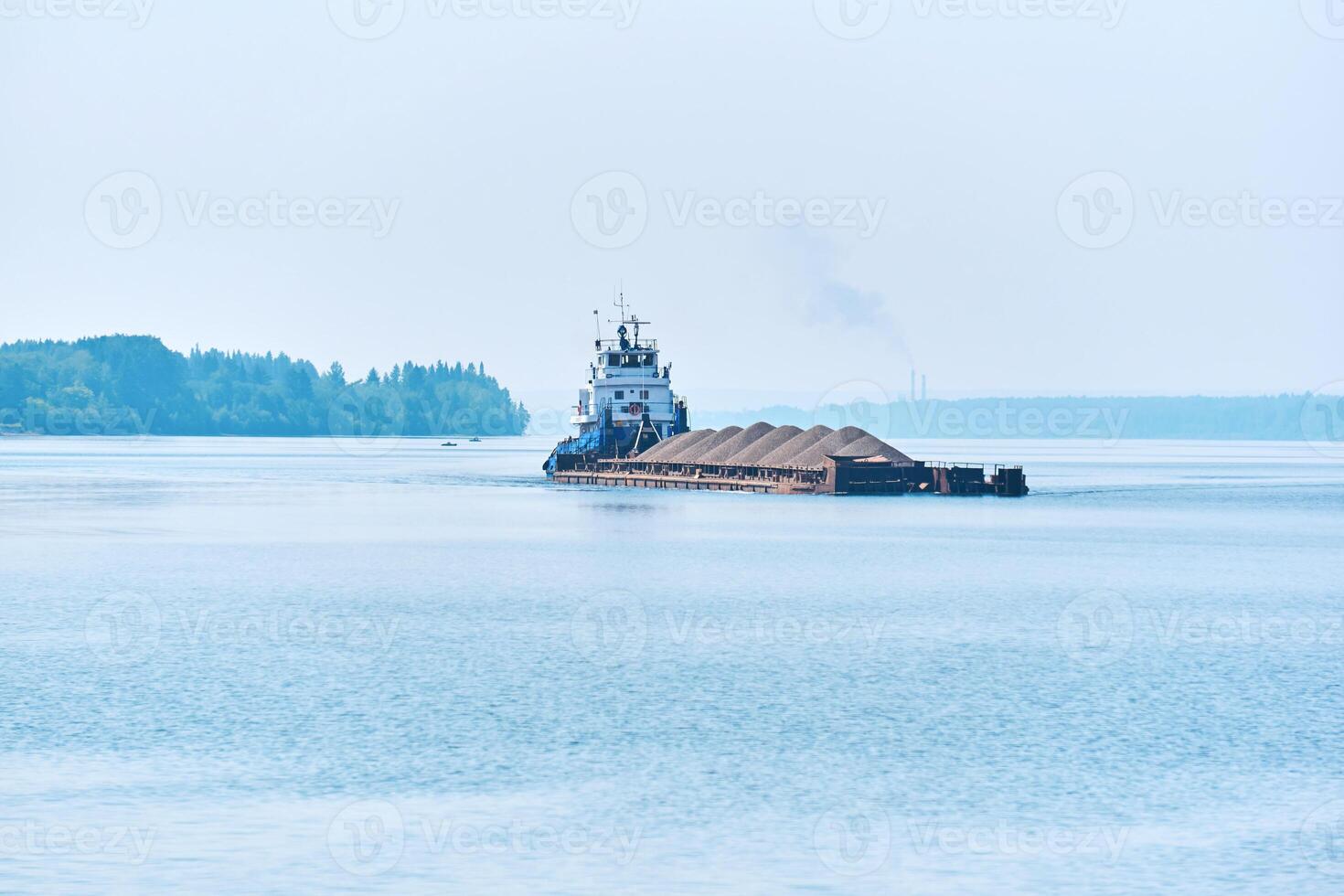 pusher tug pushes dry bulk cargo barge with sand on the river in the morning haze photo