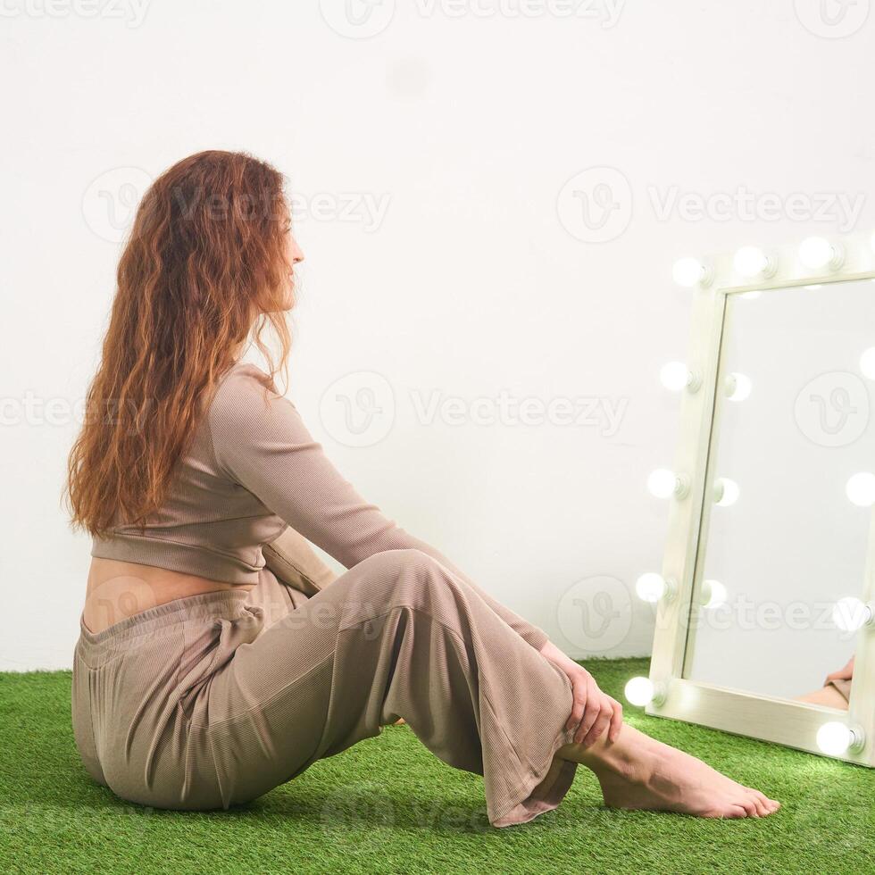 woman looks in the illuminated mirror for dressing room, sitting on the floor in the studio photo