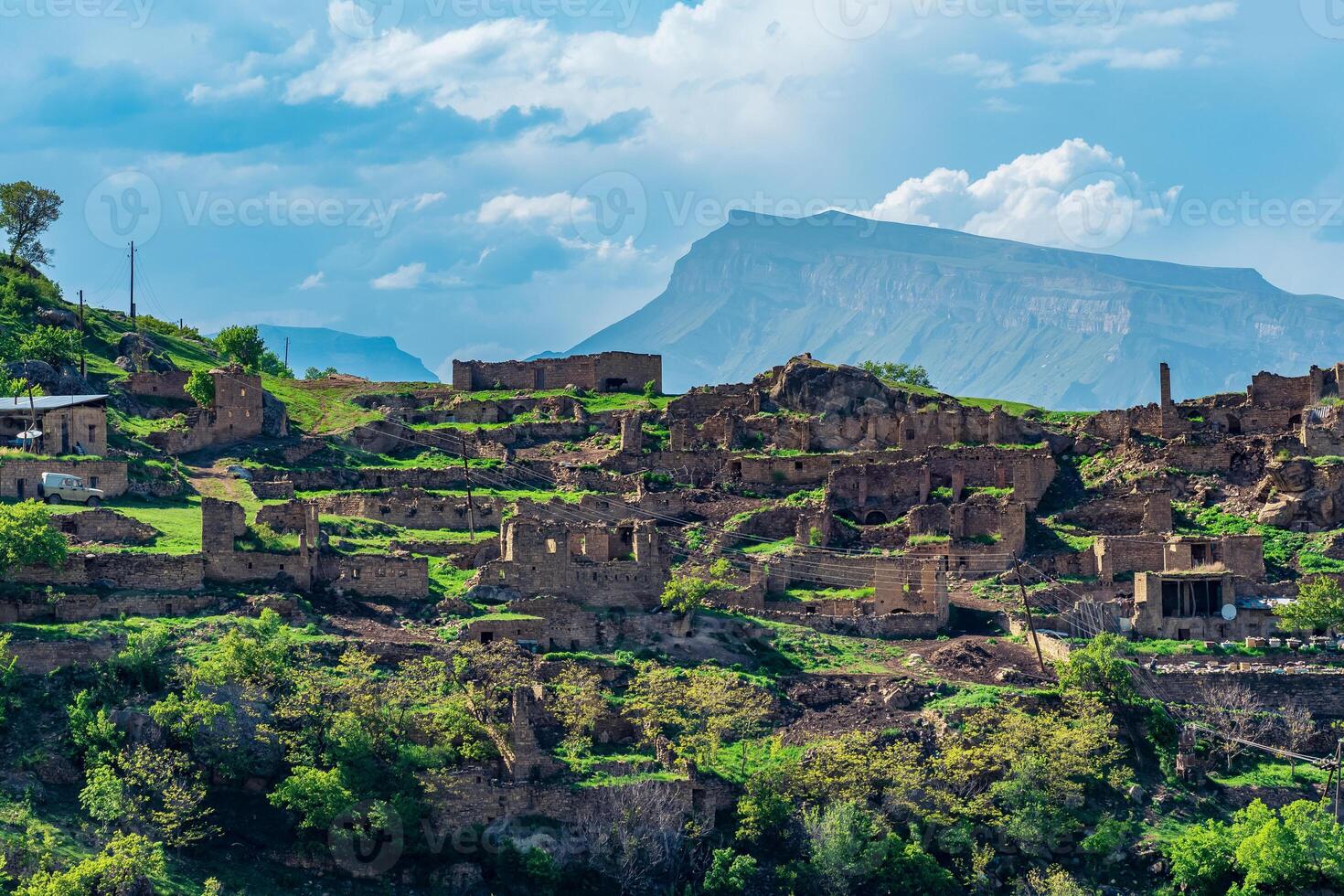 ruins of houses on a mountainside in Kurib, a depopulated village with the only remaining household with an apiary, Dagestan, another village, Chokh, is visible in the distance photo