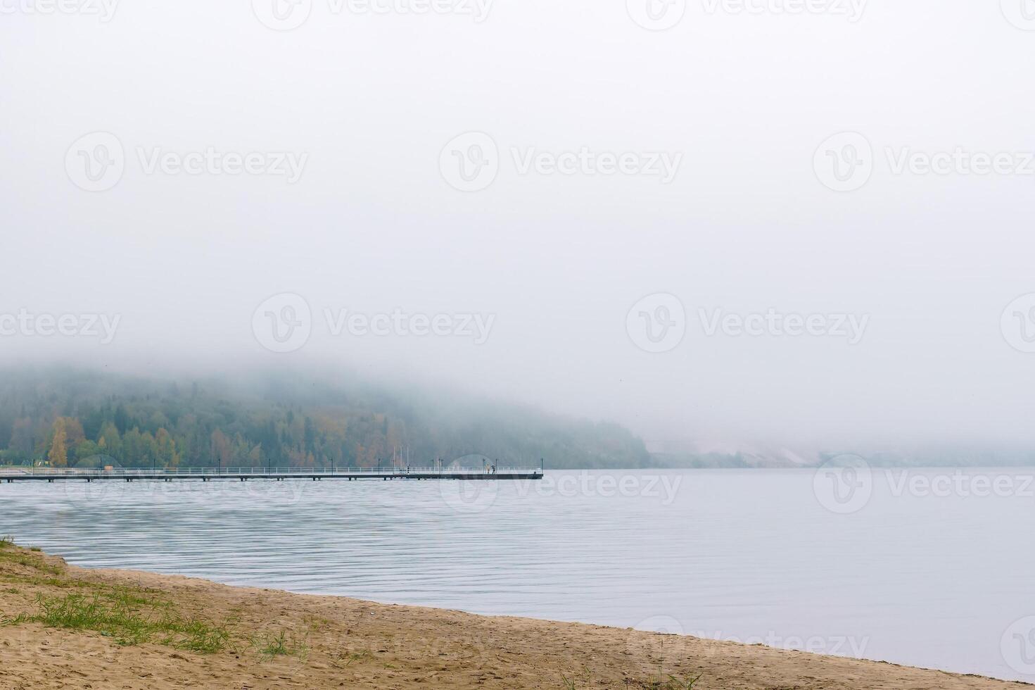 shore of an autumn lake in fog and a pier in the distance photo