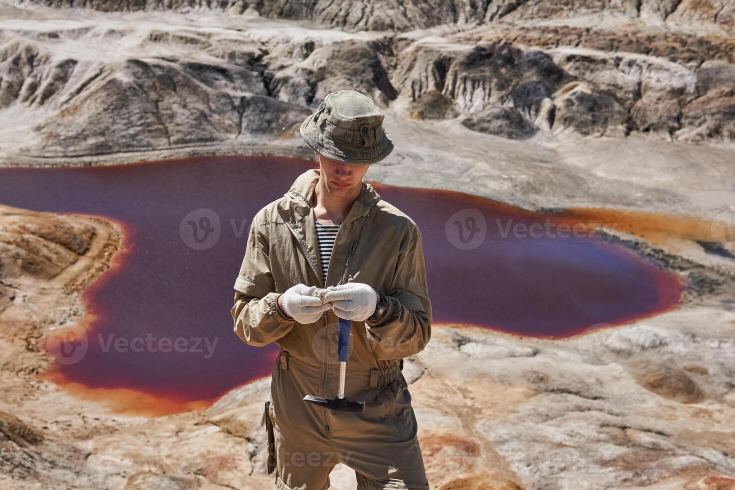 geologist examines a sample of mineral in the desert against the background of a salt lake photo