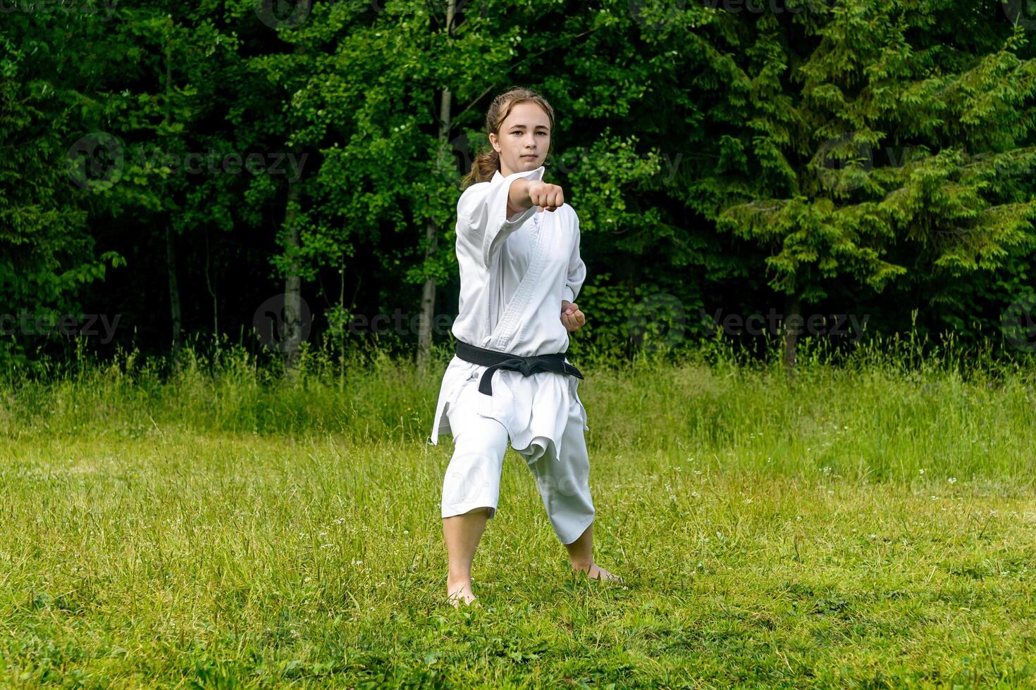 teenage girl training karate kata outdoors, performs punch seiken chudan tsuki photo