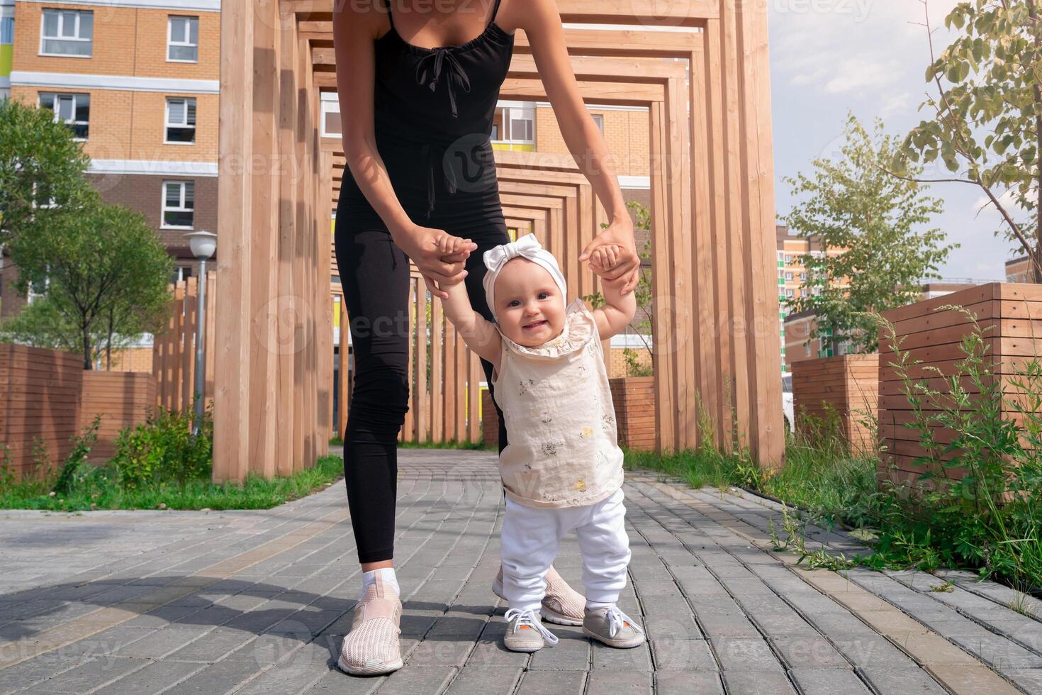 toddler baby girl with mom walk in the city courtyard, child learns to walk photo