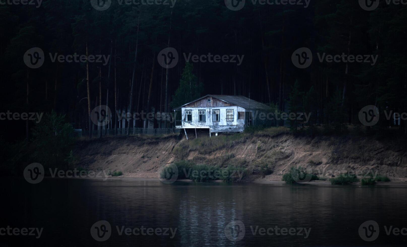 abandonado arruinado casa en un oscuro enselvado banco casi colapsado dentro el río foto