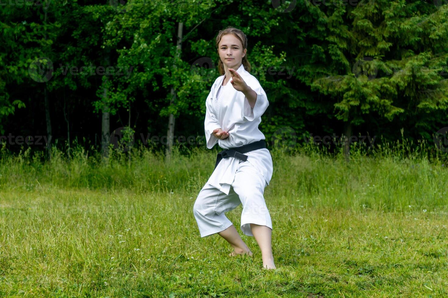 teenage girl training karate kata outdoors, performs soto uke or outside block in kakutsu dachi stand photo